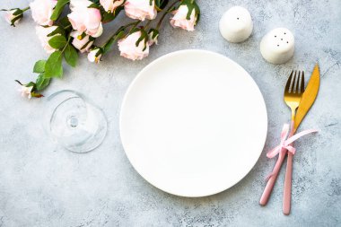 Masa seti beyaz tabak, çatal bıçak takımı ve gül çiçekli şarap kadehi. Yıldönümü ya da düğün için masa dekorasyonu. Kopyalama alanı olan düz.