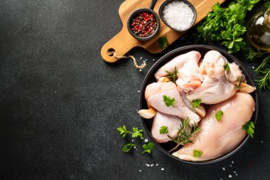 Tavuk kanatları, but ve siyah arka planda otlar ve baharatlarla göğüs. Kopyalama alanı olan üst görünüm.