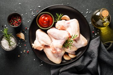 Çiğ tavuk kanadı, bitki ve domates sosu. Siyah arkaplan üzerinde düz uzandı.