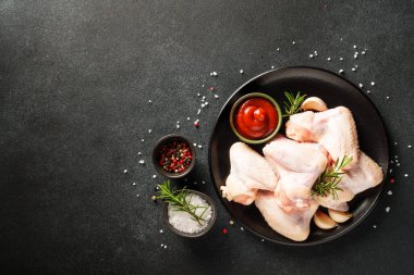 Çiğ tavuk kanadı, bitki ve domates sosu. Siyah masadaki üst görünüm.