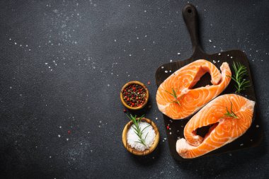 Siyah arkaplanda çiğ somon bifteği. Yemek pişirmek için malzemelerle üst görünüm.