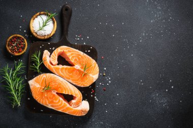 Siyah arkaplanda çiğ somon bifteği. Yemek pişirmek için malzemelerle üst görünüm.