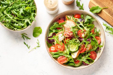 Fırında tavuk göğsü, taze salata yaprakları ve sebzeli yeşil salata. Beyaz arkaplanda üst görünüm.