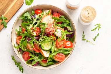 Fırında tavuk göğsü, taze salata yaprakları ve sebzeli yeşil salata. Beyaz arkaplanda üst görünüm.