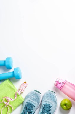 Spor ayakkabıları, dambıllar, yeşil elma ve beyaz arka planda izole edilmiş bir şişe su. Düz görünüm.