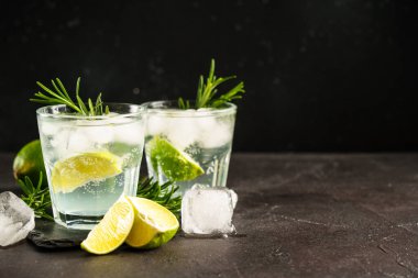 Cin toniği. Siyah zemin üzerinde cin, tonik, buz küpleri, limon ve biberiye bulunan alkol kokteyli..