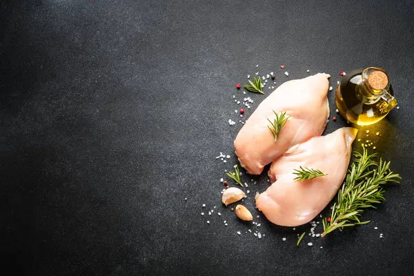 チキンミート 黒いテーブルにスパイスが付いている生の鶏の胸 トップビュー ロイヤリティフリーのストック画像
