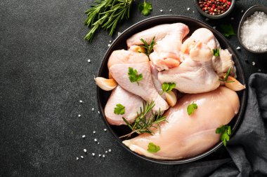 Tavuk kanatları, but ve siyah arka planda otlar ve baharatlarla göğüs. Kopyalama alanı olan üst görünüm.