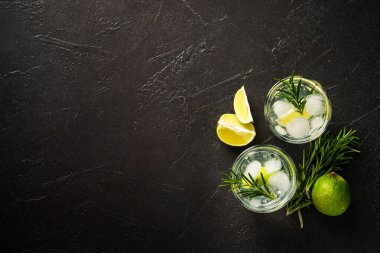 Cin toniği. Siyah arka planda cin, tonik, buz, limon ve biberiye karışımı. Kopyalama alanı olan üst görünüm.