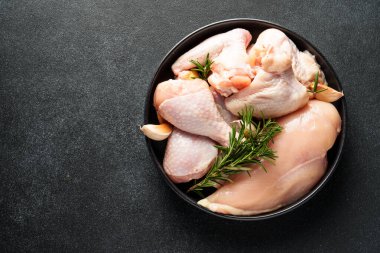 Tavuk kanatları, but ve siyah arka planda otlar ve baharatlarla göğüs. Kopyalama alanı olan üst görünüm.