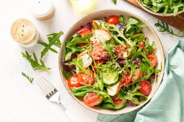 Fırında tavuk göğsü, taze salata yaprakları ve sebzeli yeşil salata. Beyaz arkaplanda üst görünüm.