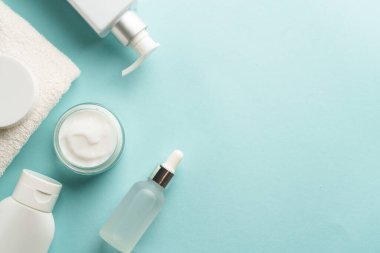Mavi üzerine cilt bakım ürünleri. Yüz kremi, tonik, serum şişesi. Kopyalama alanı olan düz resim.