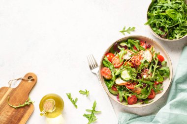 Beyaz masada sağlıklı yiyecekler. Fırında tavuk göğsü, taze salata yaprakları ve zeytinyağlı sebzeli yeşil salata. Kopyalama alanı olan üst görünüm..