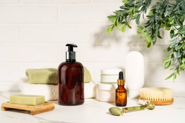 Banyoda beyaz arka planda doğal kozmetik ürünler var. Sabun, serum şişesi, yeşim taşı silindiri..