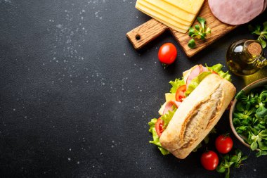 Ciabatta sandviçi, marul, peynir, domates ve jambonlu siyah mutfak masasında pişirmek için malzemeler var. Metin için boşluk olan üst görünüm.