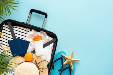 Üzerinde yazlık kumaş, ayakkabı ve aksesuarlar olan bavulu mavi arka planda aç. Yaz tatilleri, seyahat konsepti. Düz görünüm.