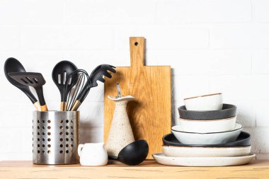 Kitchen table, kitchen utensils, cooking pots with wooden cutting board, white modern interior.