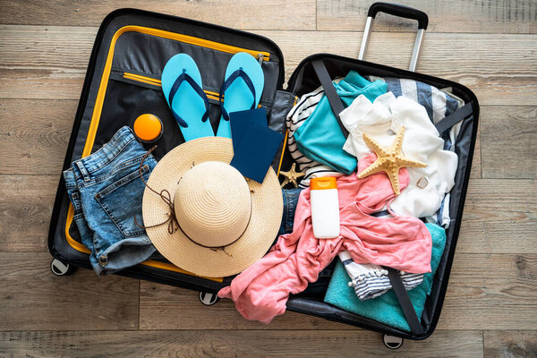 Open Suitcase with summer cloth, hat and passports. Travel concept. Flat lay image on wooden background.