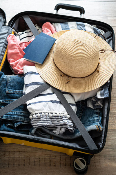 Open Suitcase with summer cloth, hat and passports. Travel concept. Flat lay image on wooden background.