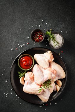 Çiğ tavuk kanadı, bitki ve domates sosu. Siyah arkaplan üzerinde düz uzandı.