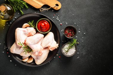 Tavuk kanatları, but ve siyah arka planda otlar ve baharatlarla göğüs. Kopyalama alanı olan üst görünüm.