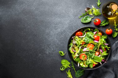 Arka planda siyah kasede salata. Sağlıklı yeşil sebze salatası, diyet menüsü. Üst görünüm.