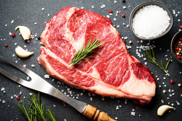 Beef steak with spices on black background. Ribeye steak raw meat. Top view.