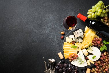 Peynir tabağı ve kırmızı şarap. Kaykay tahtasındaki üzümlü el yapımı peynir. Siyah arkaplanda üst görünüm.