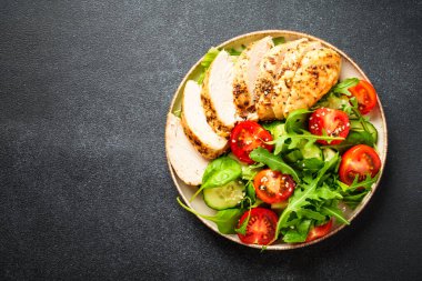 Siyah masada ızgara tavuk eti ve yeşil salata. Kopyalama alanı olan üst görünüm.