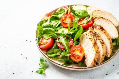 Yeşil salata, tavuk bifteği ve beyaz masada taze sebzeler..