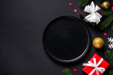 Siyah tabaklı bir Noel sofrası, siyah arka planda hediyeler ve tatil süslemeleri. Metin için boşluk ile düz uzandı.