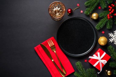 Siyah tabak, çatal bıçak takımı, hediyeler ve siyah arka planda tatil süslemeleri olan bir Noel masası. Metin için boşluk ile düz uzandı.