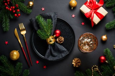 Siyah arka planda Noel yemeği. Siyah tabak, şarap kadehi, çatal bıçak takımı ve bayram süslemeleriyle şenlik masası. Düz yatıyordu.