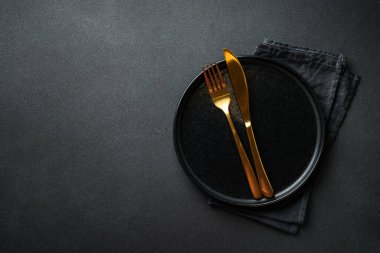 Altın çatal bıçaklı siyah tabak. Modern moda yemekler. Siyah arkaplanda düz uzandı.