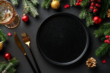 Noel sofrası. Noel yemeği. Siyah arka planda siyah tabaklar, çatal bıçak takımı ve süslemeler. Kopyalama alanı olan düz.