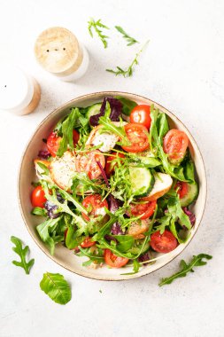 Fırında tavuk göğsü, taze salata yaprakları ve sebzeli yeşil salata. Beyaz arkaplanda üst görünüm.