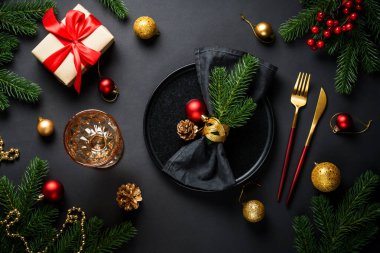 Siyah arka planda Noel yemeği. Noel sofrasında tabak, şarap kadehi, altın çatal bıçak takımı ve bayram süslemeleri..