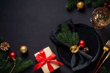 Siyah arka planda Noel yemeği. Noel sofrasında tabak, şarap kadehi, altın çatal bıçak takımı ve bayram süslemeleri..