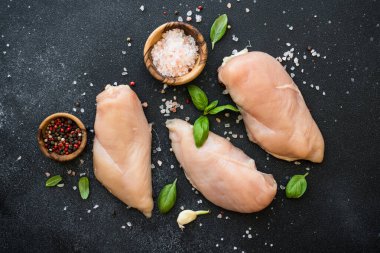 Tavuk fileto, çiğ tavuk göğsü, baharat ve siyah arka planda bitkiler. Metin için boşluk olan üst görünüm.