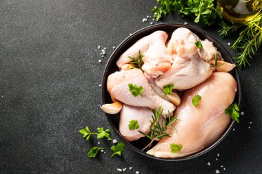 Tavuk kanatları, but ve siyah arka planda otlar ve baharatlarla göğüs. Kopyalama alanı olan üst görünüm.