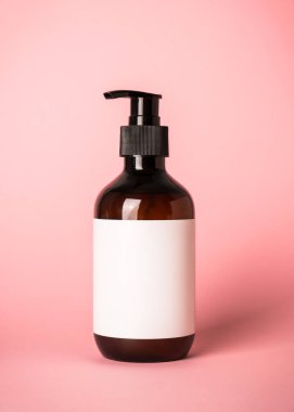 Pembe arka planda pompalı şampuan şişesi ve havlular..