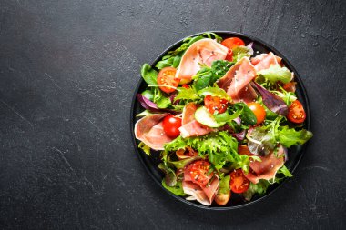 Siyah arka planda yeşil salata. Yeşil salata yaprakları, tütsülenmiş et ve domates. Metin için boşluk olan üst görünüm.