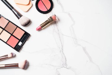 Beyaz mermer arka planda güzellik ürünleri uydur. Kozmetik palet, fırçalar ve pembe ruj. Kopyalama alanı olan üst görünüm.