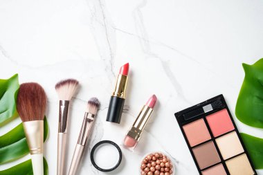 Beyaz mermer arka planda çiçekli ürünler uydur. Kozmetik palet, fırçalar ve rujlar. Kopyalama alanı olan üst görünüm.