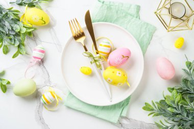 Beyaz arka planda Paskalya sofrası. Beyaz tabak, çatal bıçak takımı ve paskalya süslemeleri. Düz yatıyordu.