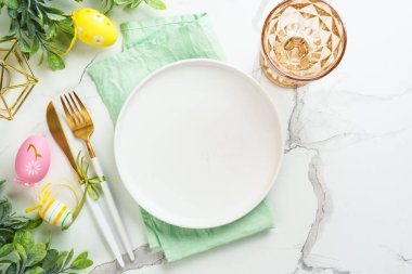 Beyaz arka planda Paskalya sofrası. Beyaz tabak, çatal bıçak takımı ve paskalya süslemeleri. Düz yatıyordu.