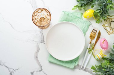 Paskalya yemeği geçmişi. Beyaz tabak, altın çatal bıçak, cam ve renkli paskalya süslemeleri. Üst görünüm.