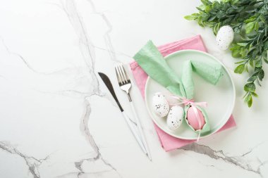 Paskalya kompozisyonu. Tatil masası süslemeleri, beyaz tabak, altın çatal bıçak, cam ve renkli paskalya yumurtaları. Üst görünüm.