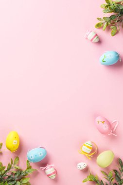 Paskalya yumurtaları ve yeşil yapraklar pembe arka planda. Kopyalama alanı olan düz, dikey.
