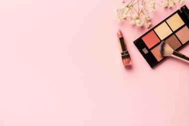 Pembe arka planda fotokopi alanı olan ürünler yap. Makyaj paleti ve çiçekli ruj.